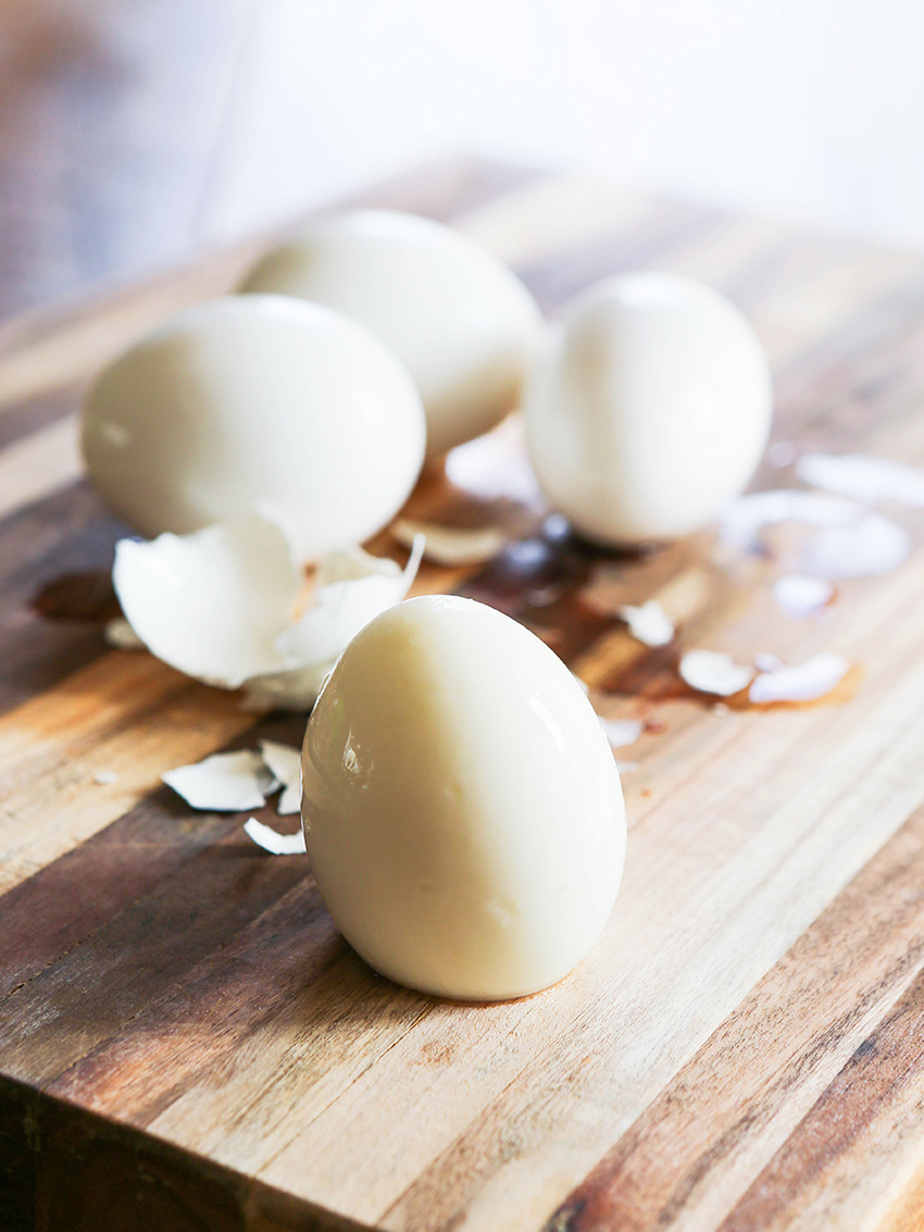 A peeled, perfect hard boiled egg sitting in front of the shells and 3 eggs with the shell on