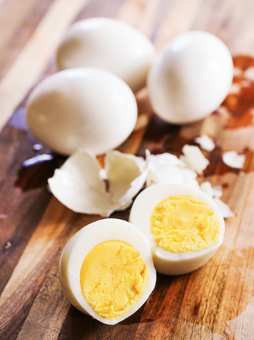 3 eggs in the shell with shells peeled off an egg in front of them with the hard boiled egg cut in half in front