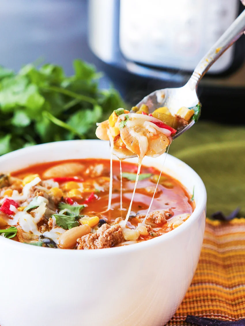  Spoon of chili being pulled from bowl and sitting next to Instant Pot 
