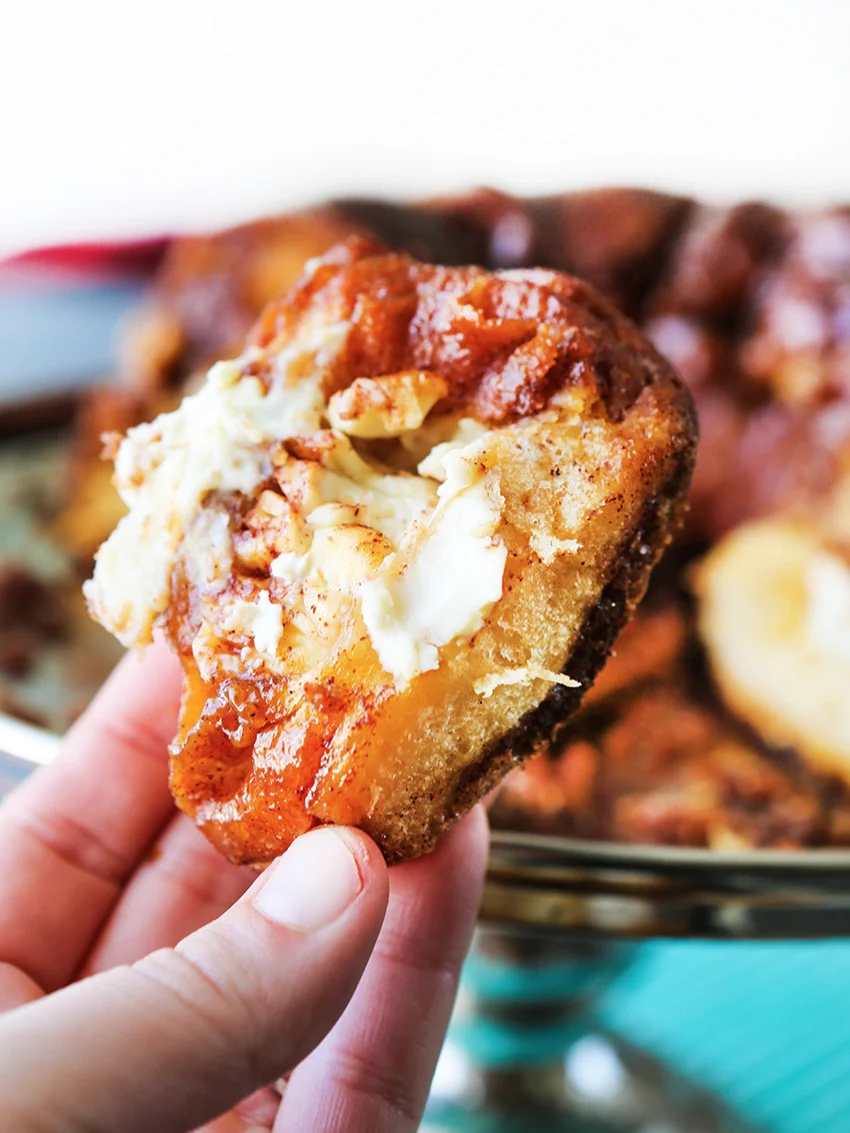 Fingers holding piece of bread with cream cheese oozing out