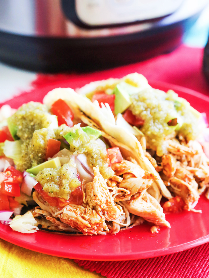 Two chicken tacos on a plate with toppings 