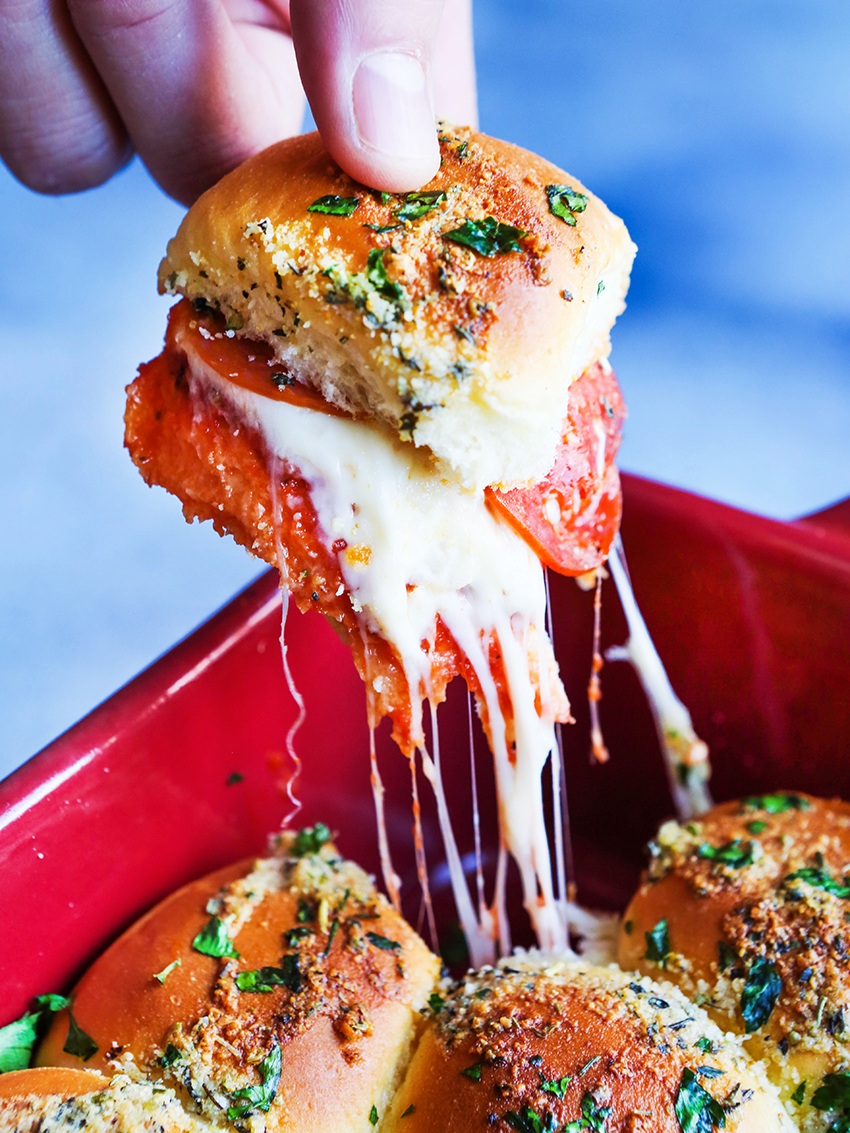 fingers pulling a cheesy pizza slider out of a pan