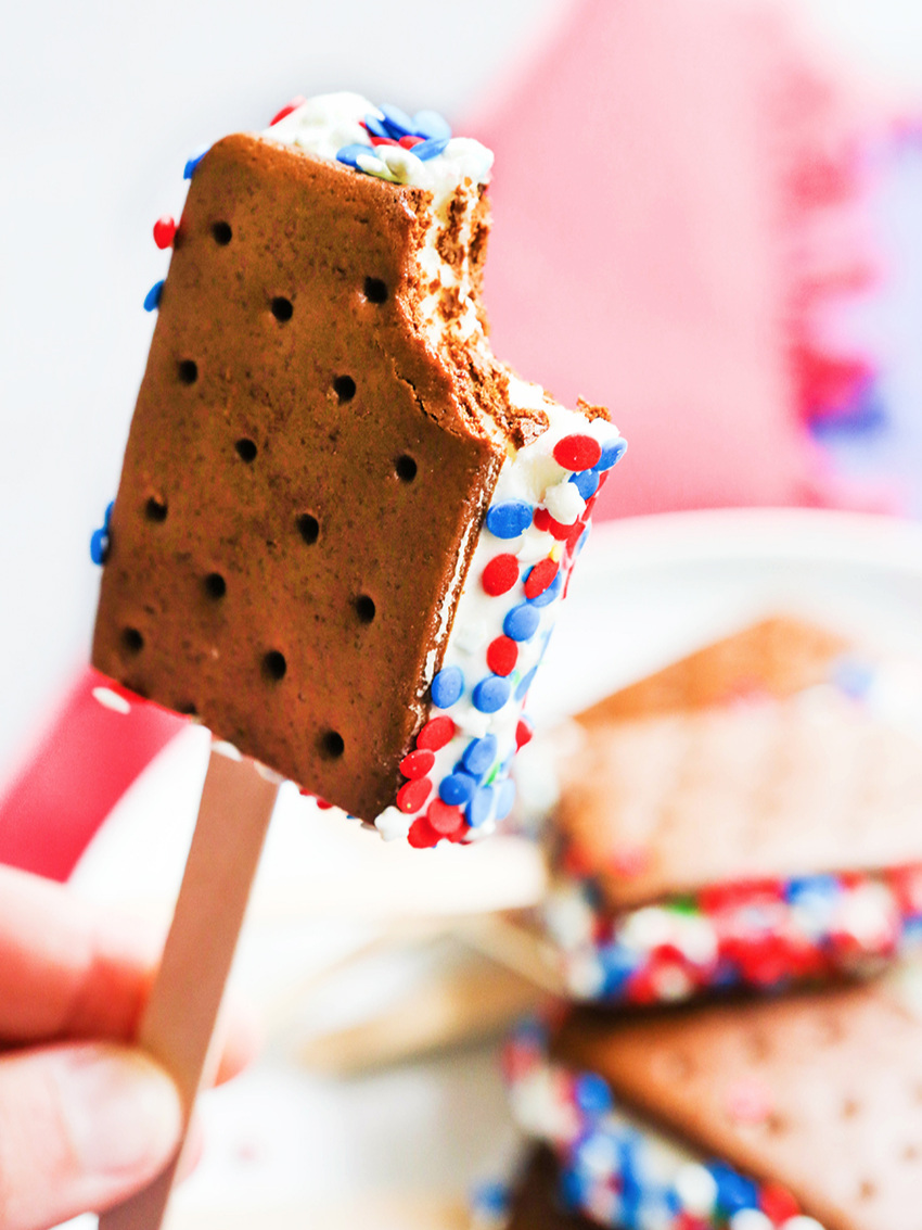 Hand holding an ice cream sandwich with a bite out of it with sprinkles 4th of july dessert