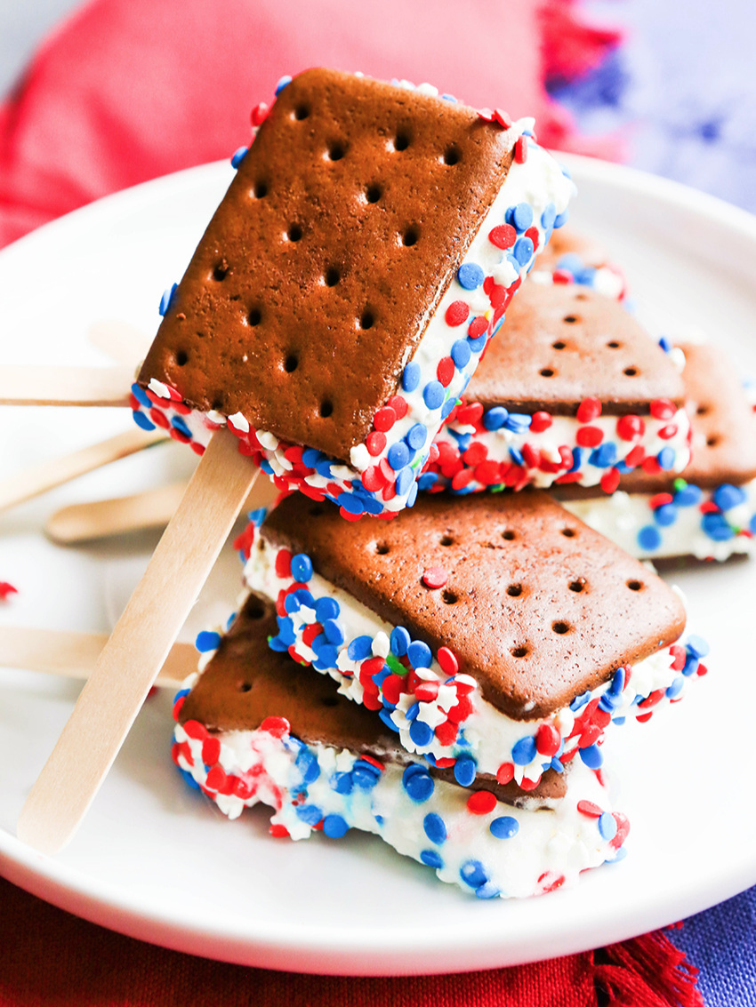 Ice cream sandwiches with red, white and blue sprinkles on a stick on top of one another on a plate. 