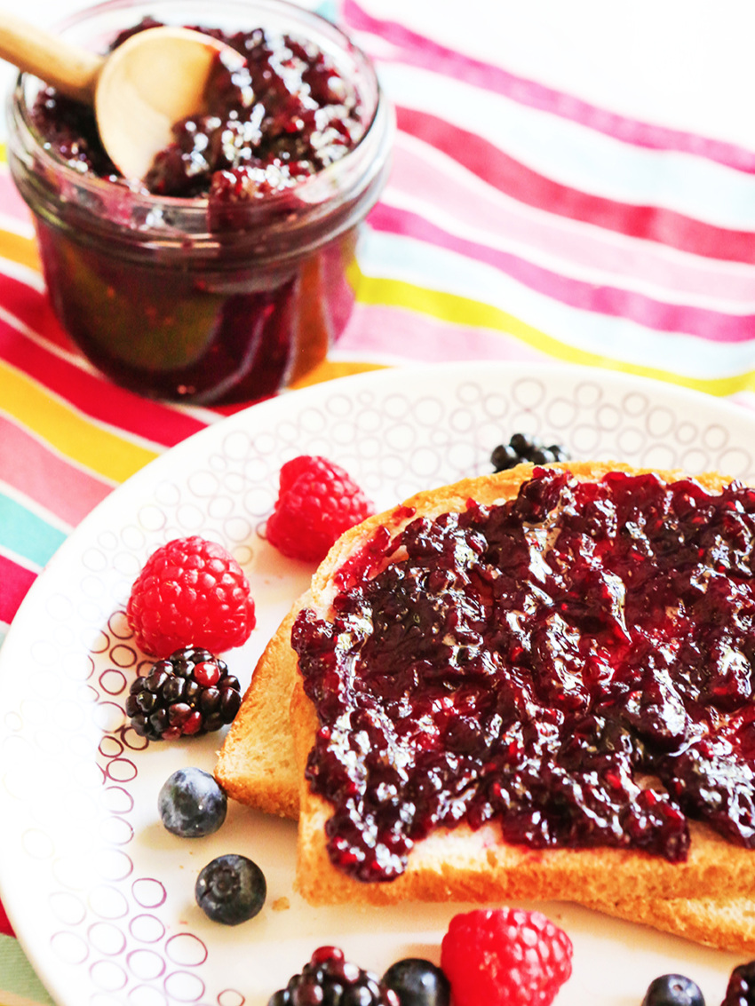 Slice of bread with mixed berry jam spread across on a plate with fresh berries around the plate 
