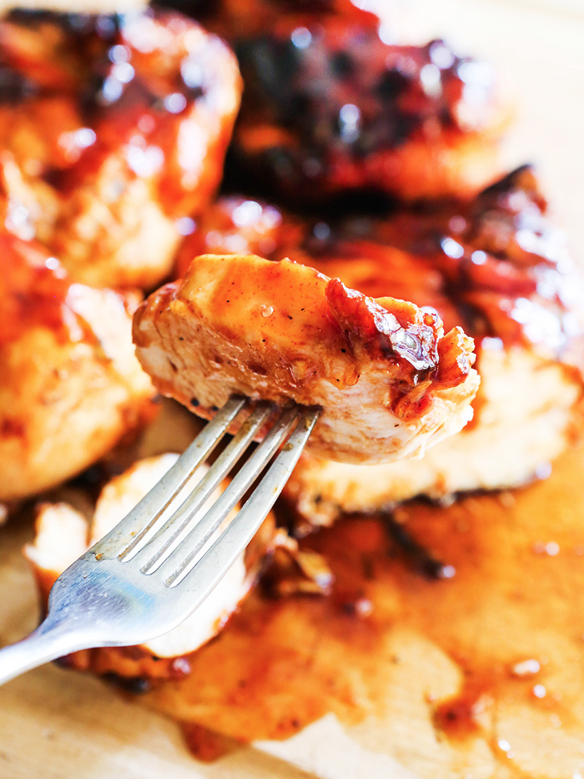 Close up of fork and a piece of chicken with BBQ sauce on it, the rest of the chicken in the background. 
