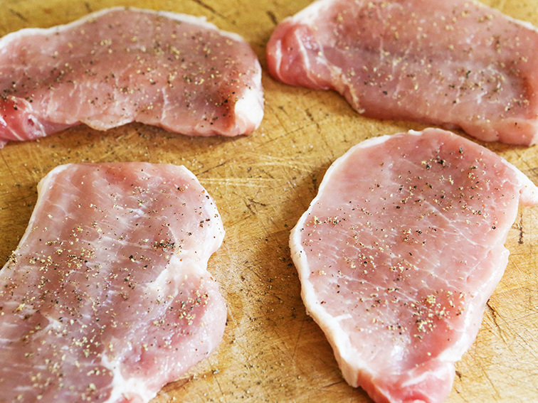 Four pork chops on cutting board with salt and pepper 