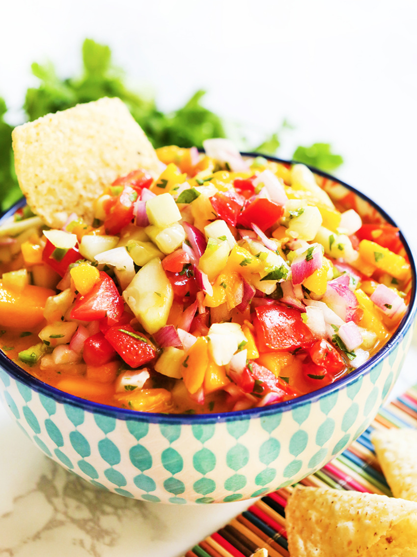 bowl of salsa with tomatoes and mangoes next to pile of chips