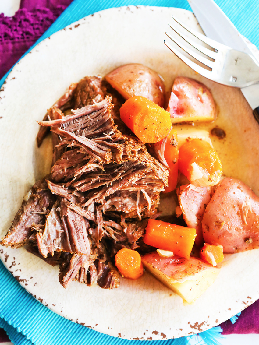 Plate of shredded beef with potatoes and carrots next to it.