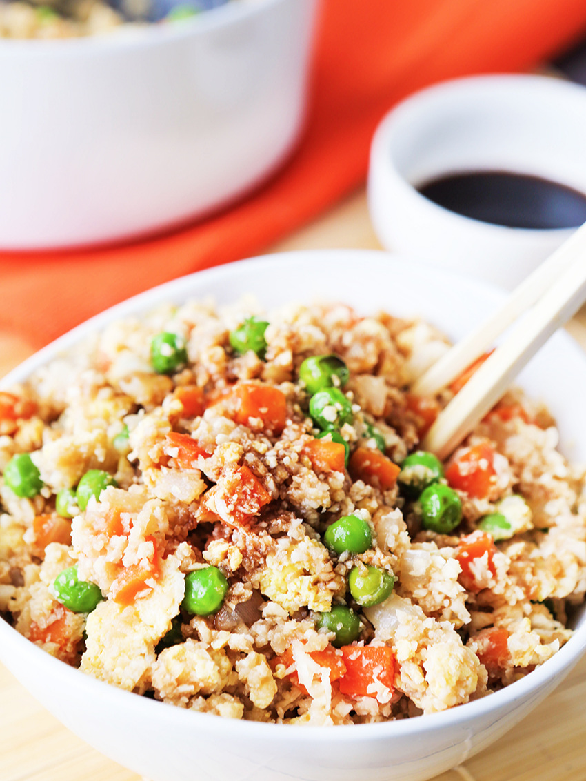 chopsticks stuck into a bowl of fried rice with peas and carrots