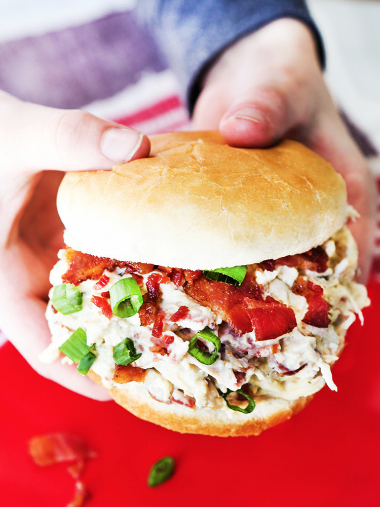 Hands holding a loaded sandwich with chicken, bacon and green onions.