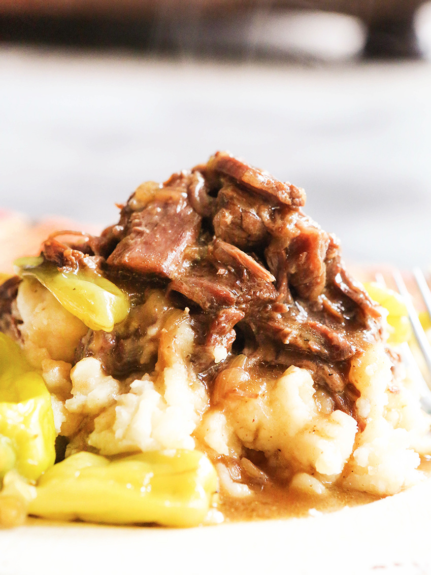 Close up of instant pot mississippi pot roast over a bed of mashed potatoes with pepperonicinis