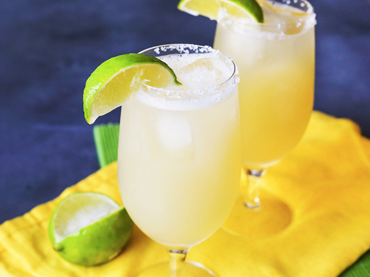 two margarita glasses next to each other with lime wedges stuck in glasses