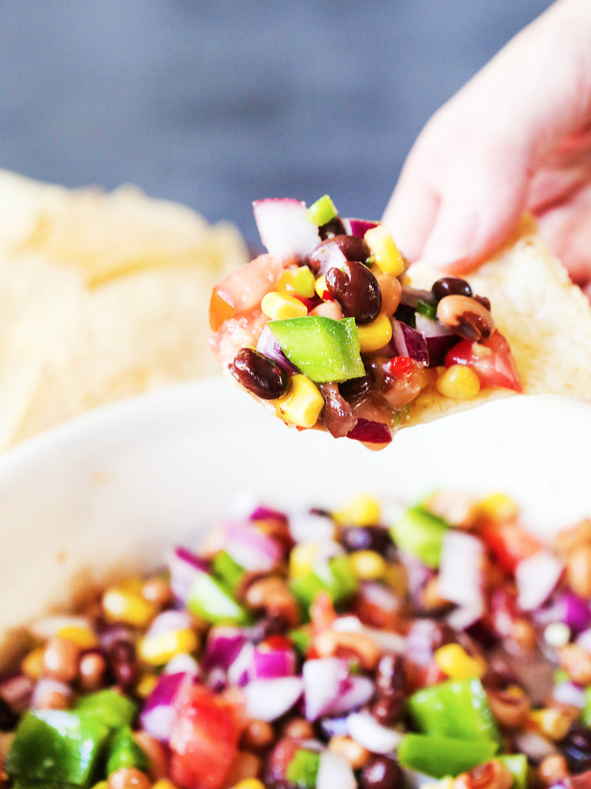 fingers holding chip full of chunky salsa over serving bowl