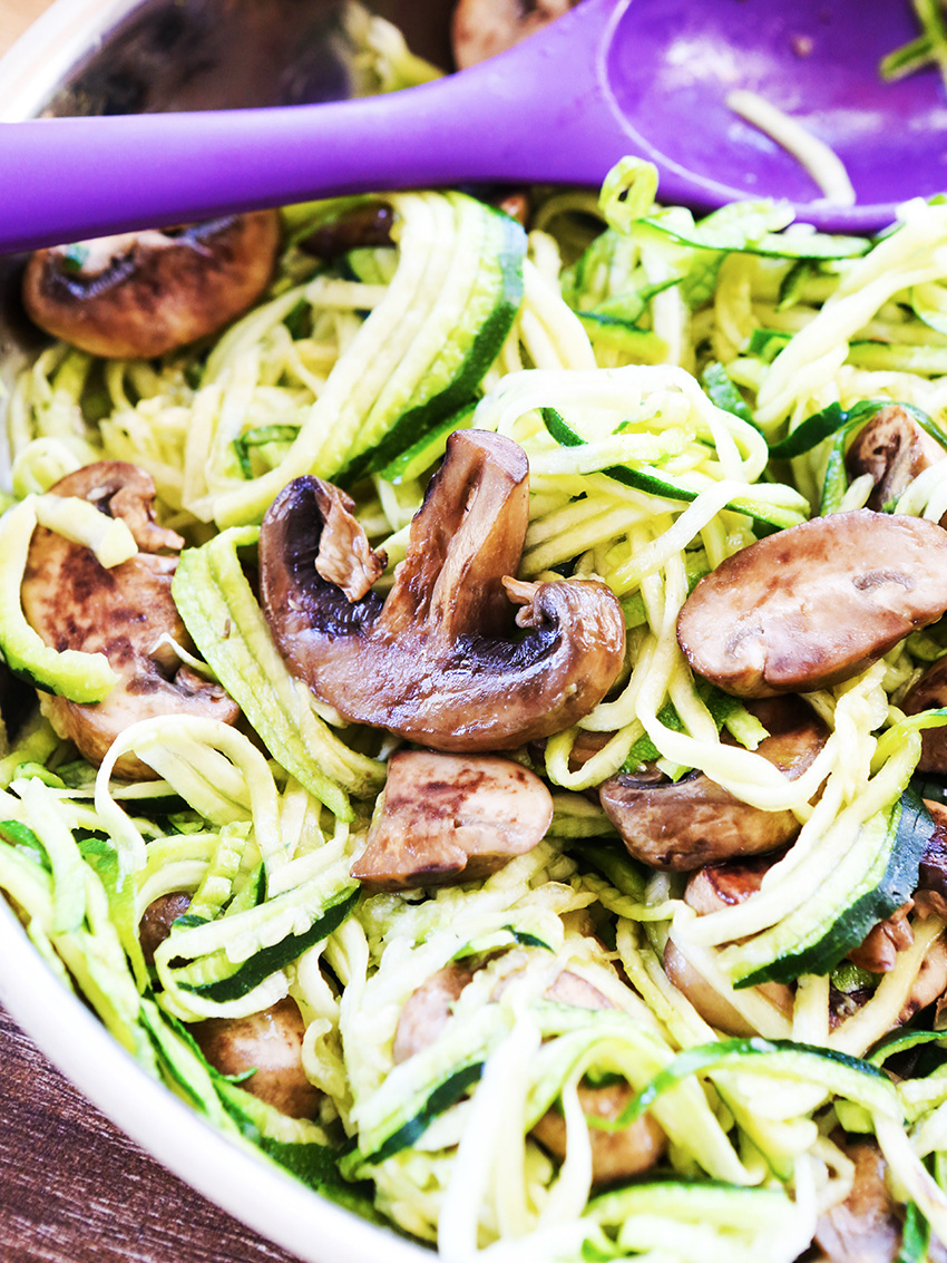 close up of zoodles and mushrooms in pan with mixing spoon