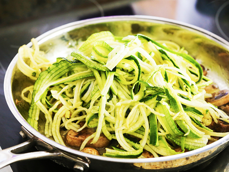 spiralized zucchini in skillet ready to be sauteed