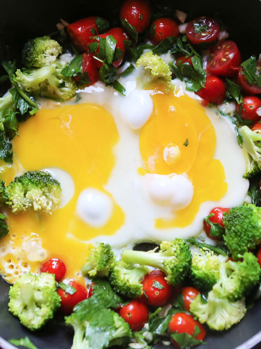 Eggs cooking in a skillet with veggies surrounding them