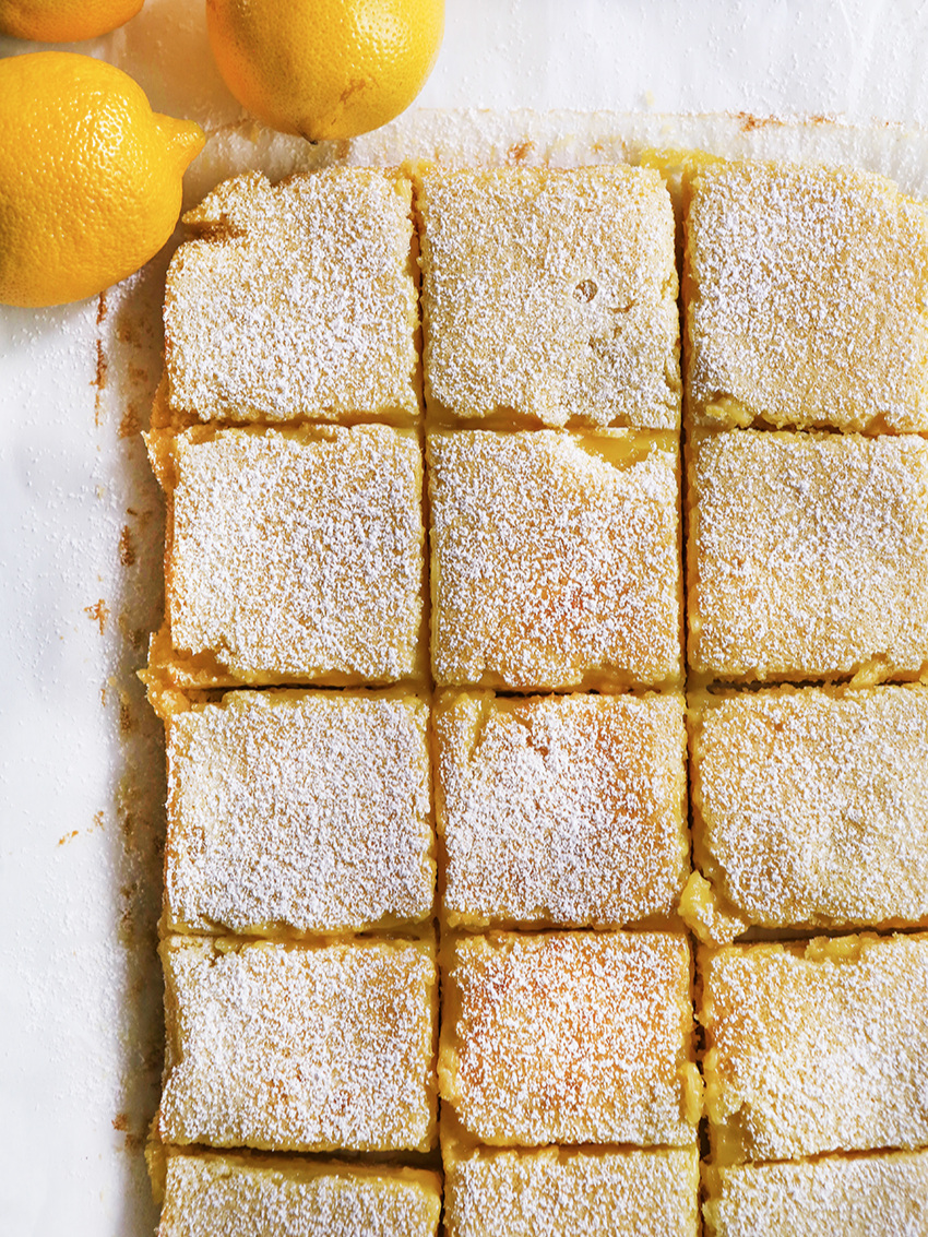Top view of lemon bars cut into squares with a lemon at the top 