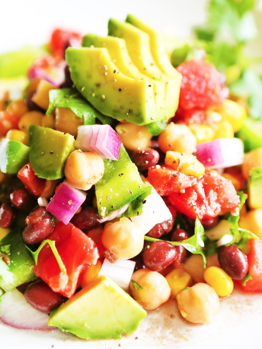 close up of colorful loaded veggie salad on plate and topped with avocado slices