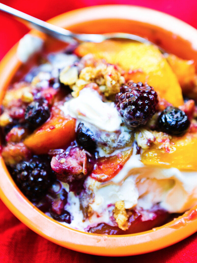 Spoon in a bowl of peach blueberry crisp with melted ice cream