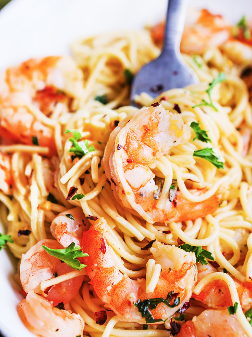 This photo shows a white plate filled with Shrimp Scampi with a fork, ready to eat.