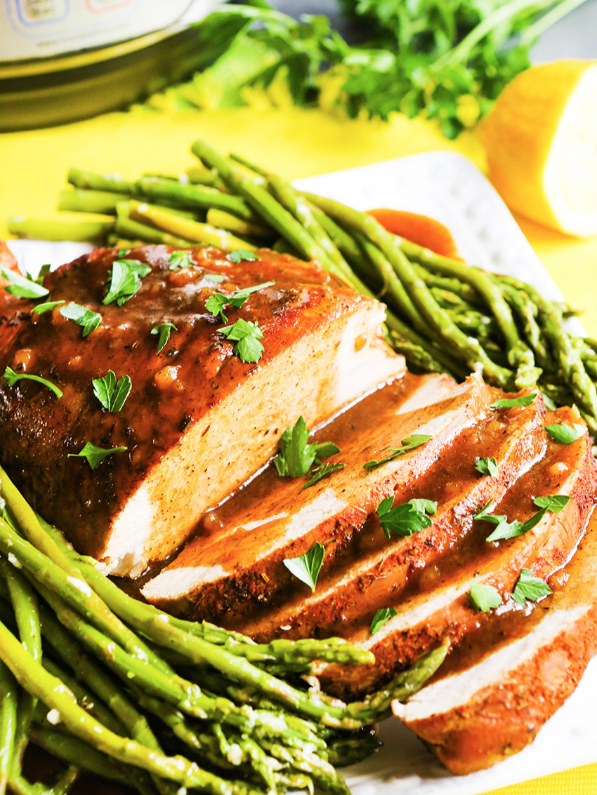 Instant Pot Turkey Breast on platter with asparagus next to pressure cooker 