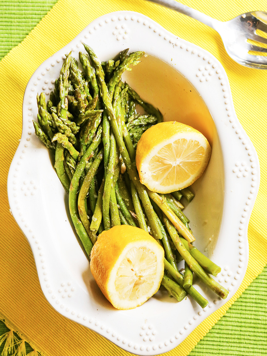 Top view of serving bowl full of instant pot asparagus and lemon halves 
