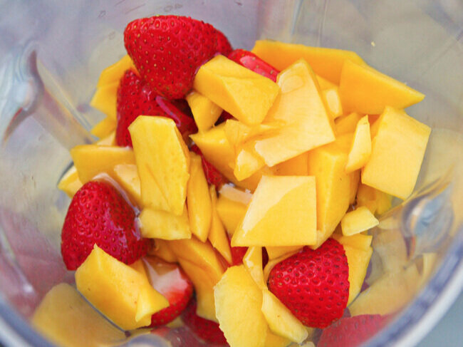Mango and strawberry pieces in a blender 