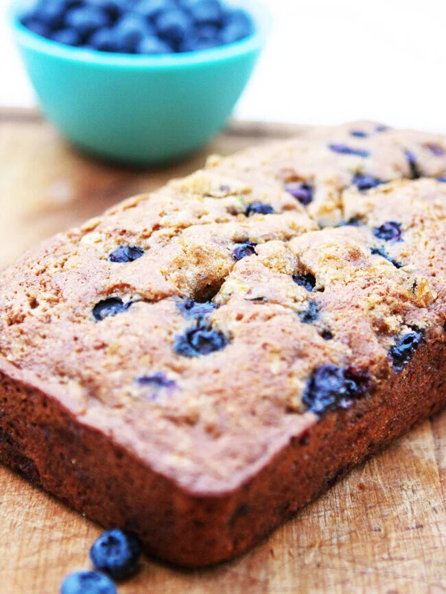  Loaf of blueberry zucchini bread sitting next to bowl of blueberries 