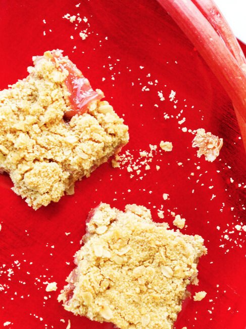  Top view of two rhubarb crunch bars on a shiny red plate 