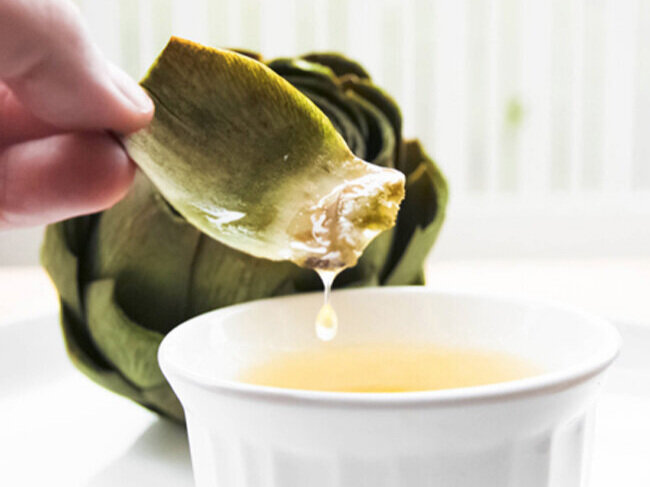hand holding artichoke leaf dripping with butter 