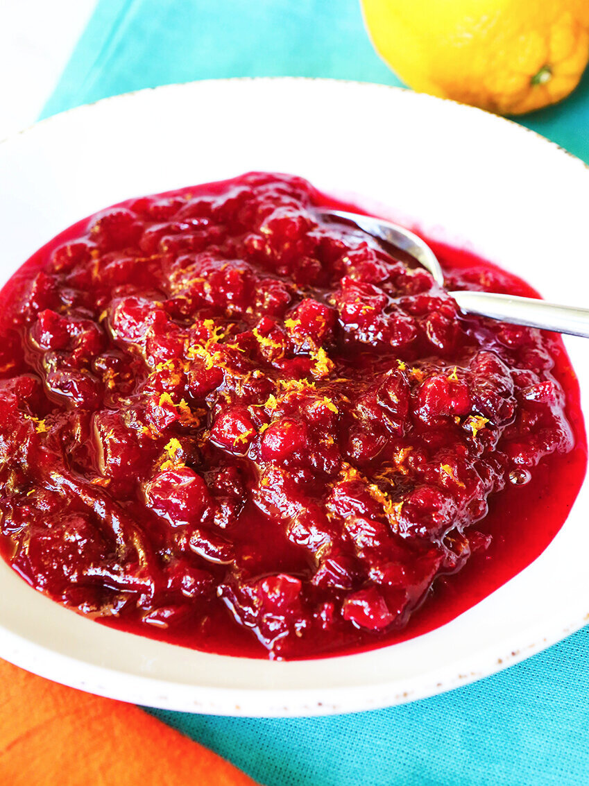  White bowl filled with cranberry sauce with zested orange in background 