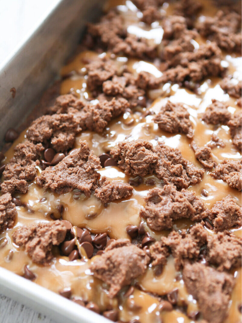 Brownie batter dropped over caramel in baking pan 