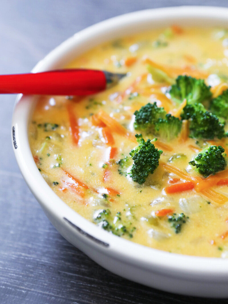  close up of bowl of broccoli cheese soup with red spoon 