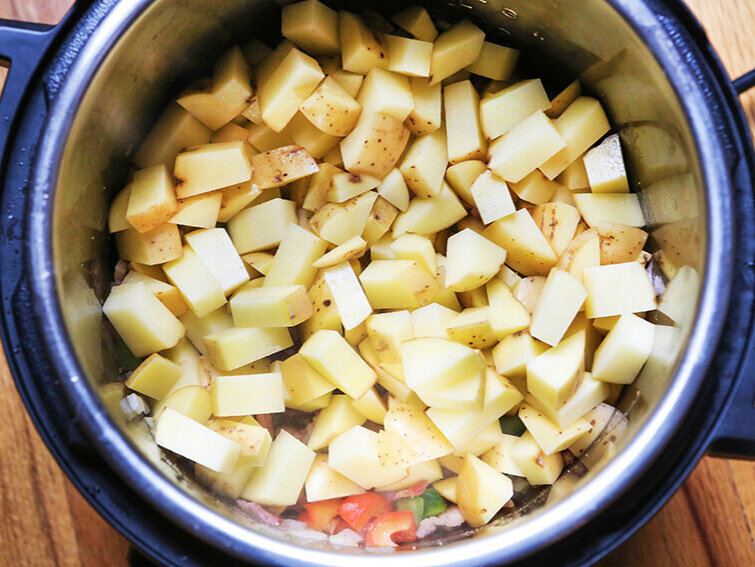 Potato pieces over veggies in Instant Pot ready to cook
