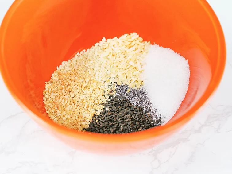 Spices in orange bowl ready to mix to create bagel seasoning 
