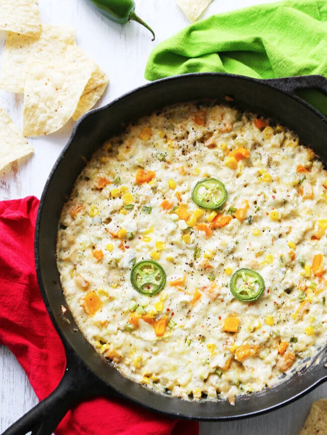  top view of cast iron pan of corn and crab dip next to red placemat 