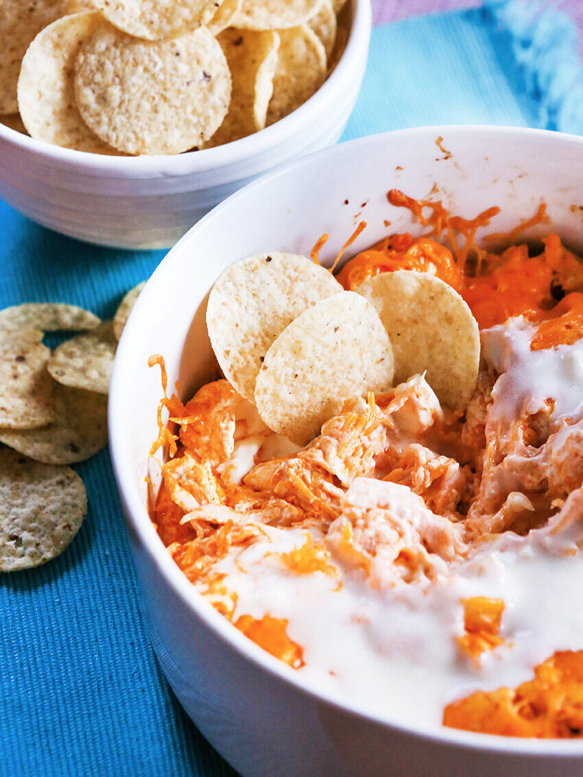 Pan of buffalo chicken dip with tortilla chips next to bowl