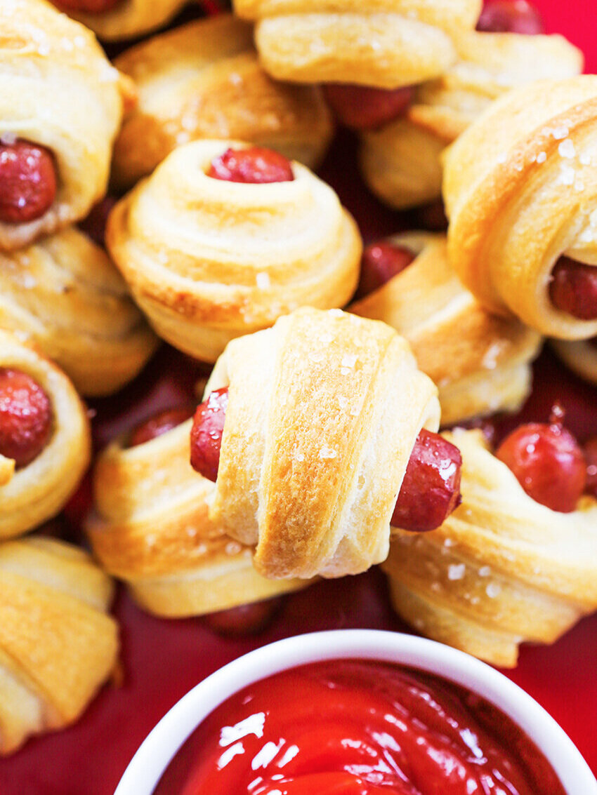looking down on heaping pile of pigs in a blanket with ketchup side 