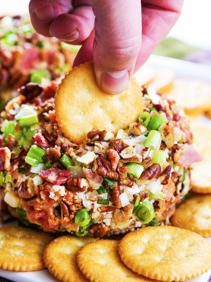 Hand dipping cracker into ball of cheese