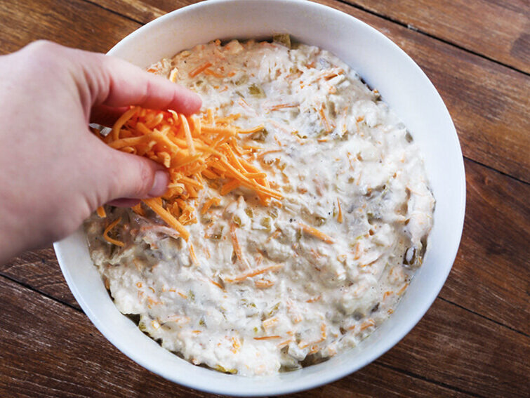 Handful of shredded cheddar being spread over top of dip