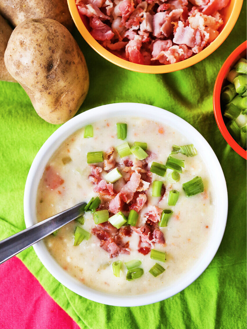 Bowl of potato soup sitting next to bowls of toppings 