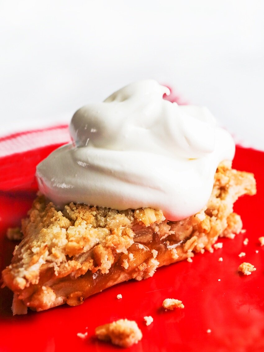  Slice of apple pie on a red plate with heaping pile of whipped cream on top 