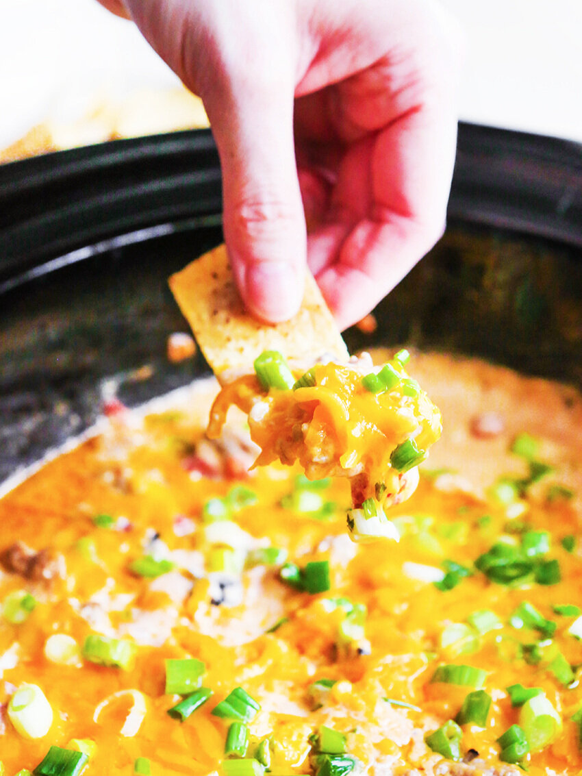  Hand pulling chip full of sausage cheese dip out of crockpot 