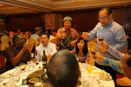 Prof Wong (centre, standing) and Dr Seah (right, in blue shirt)) raise their glasses.