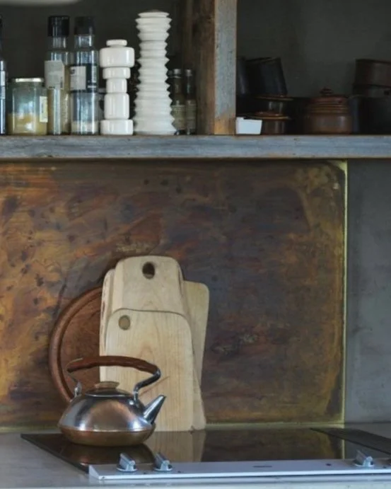 Kjøkkenmiljø med tre skjærebrett, metallkanel på komfyr, hyller med krydderkrukker og annet kjøkkenutstyr.