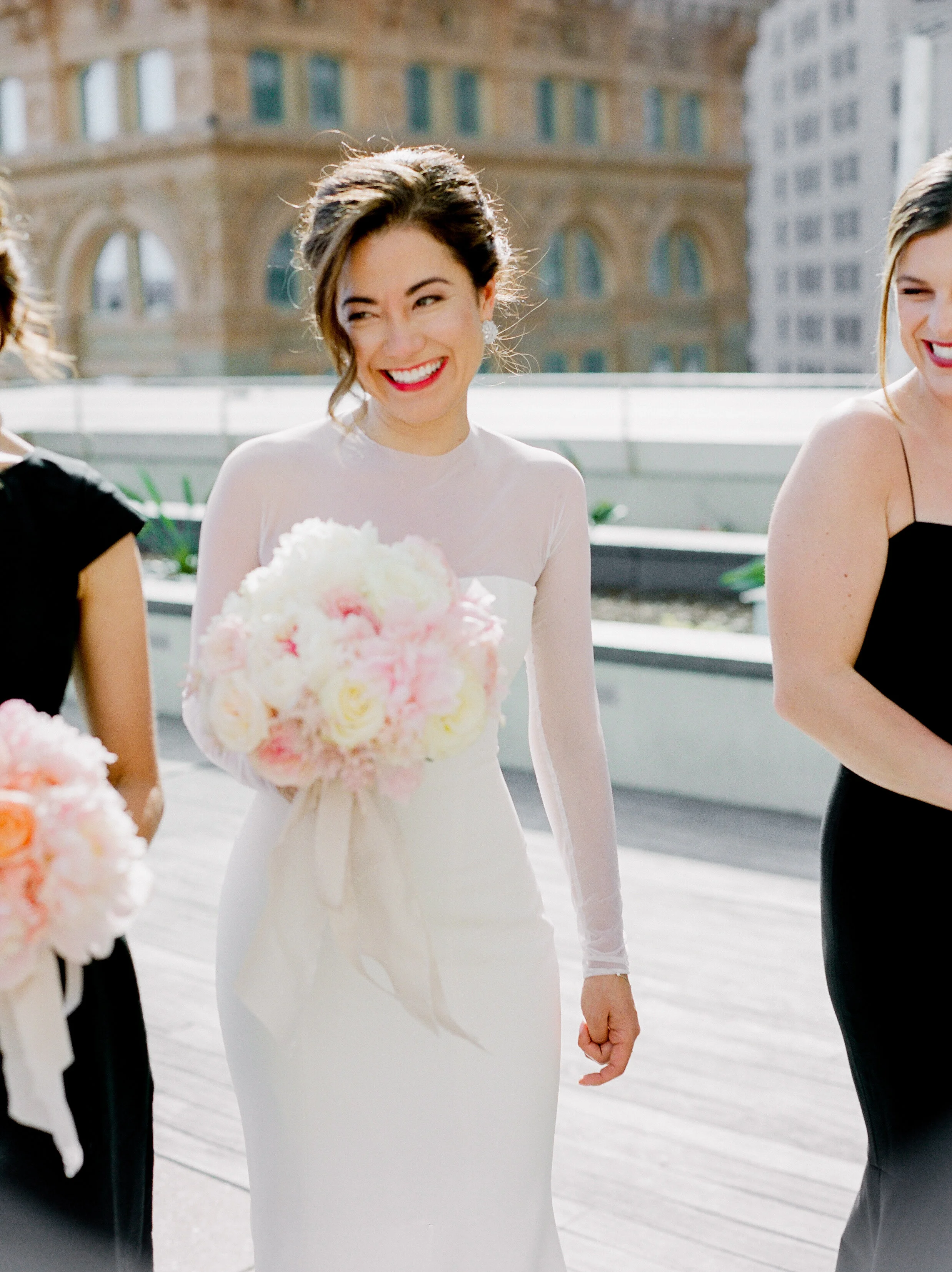 bride smiling pink peony bouquet simple wedding dress black bridesmaids dress