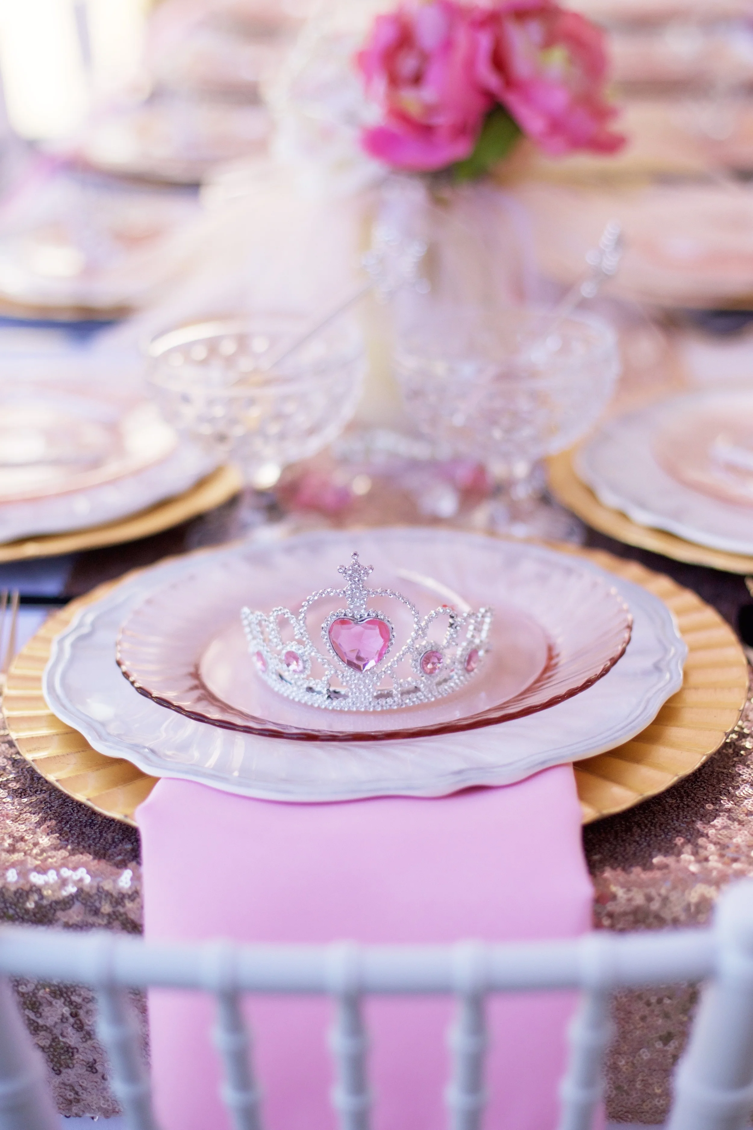 A rental collection with an elaborate ensemble of pink tutu centerpieces, white chiavari chairs, glittery runners, pink and white flowers, and sparkling tiaras that will dazzle even a Queen!