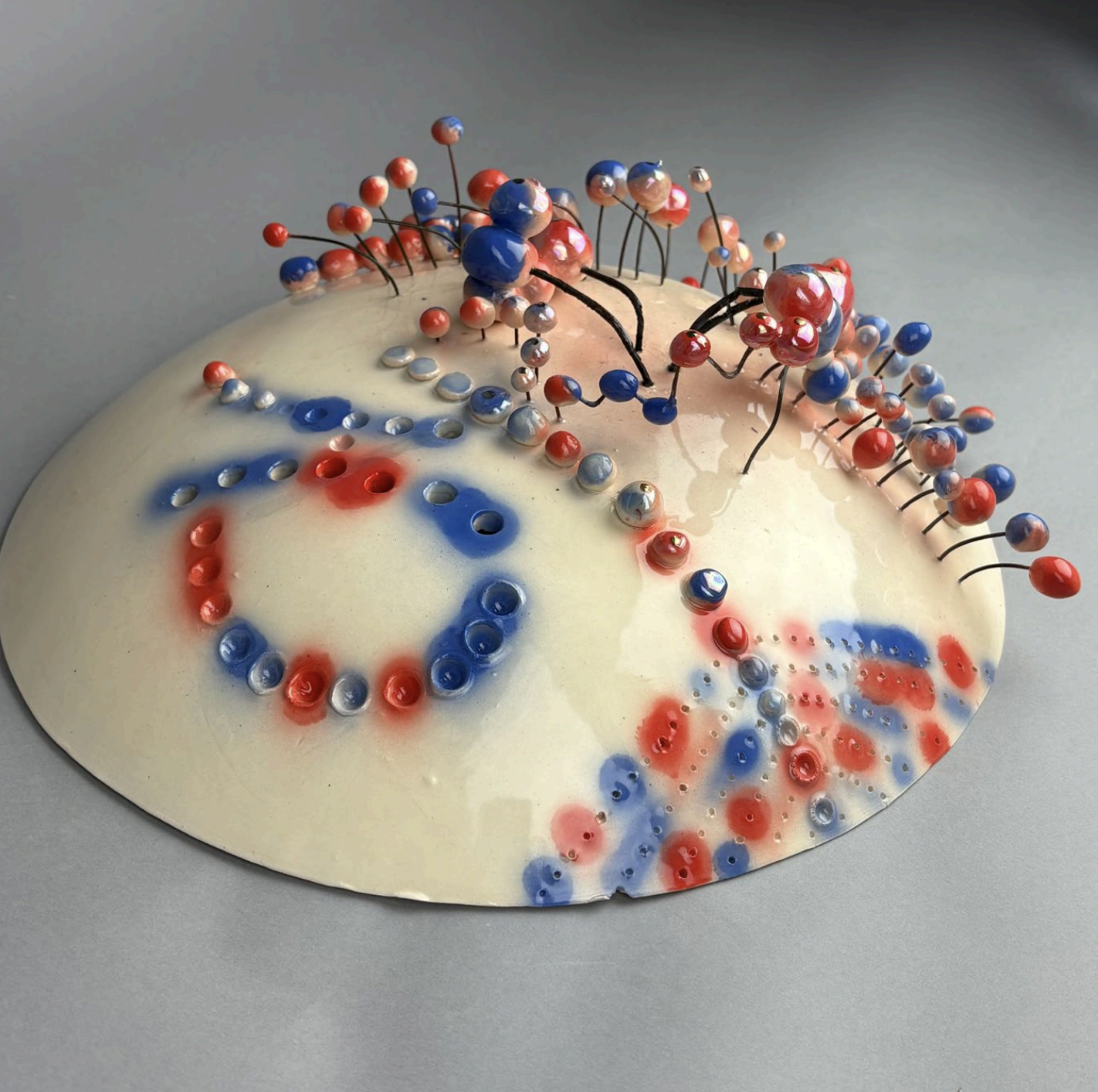 A clay shield painted blue and red with spherical projections on rods sticking up.