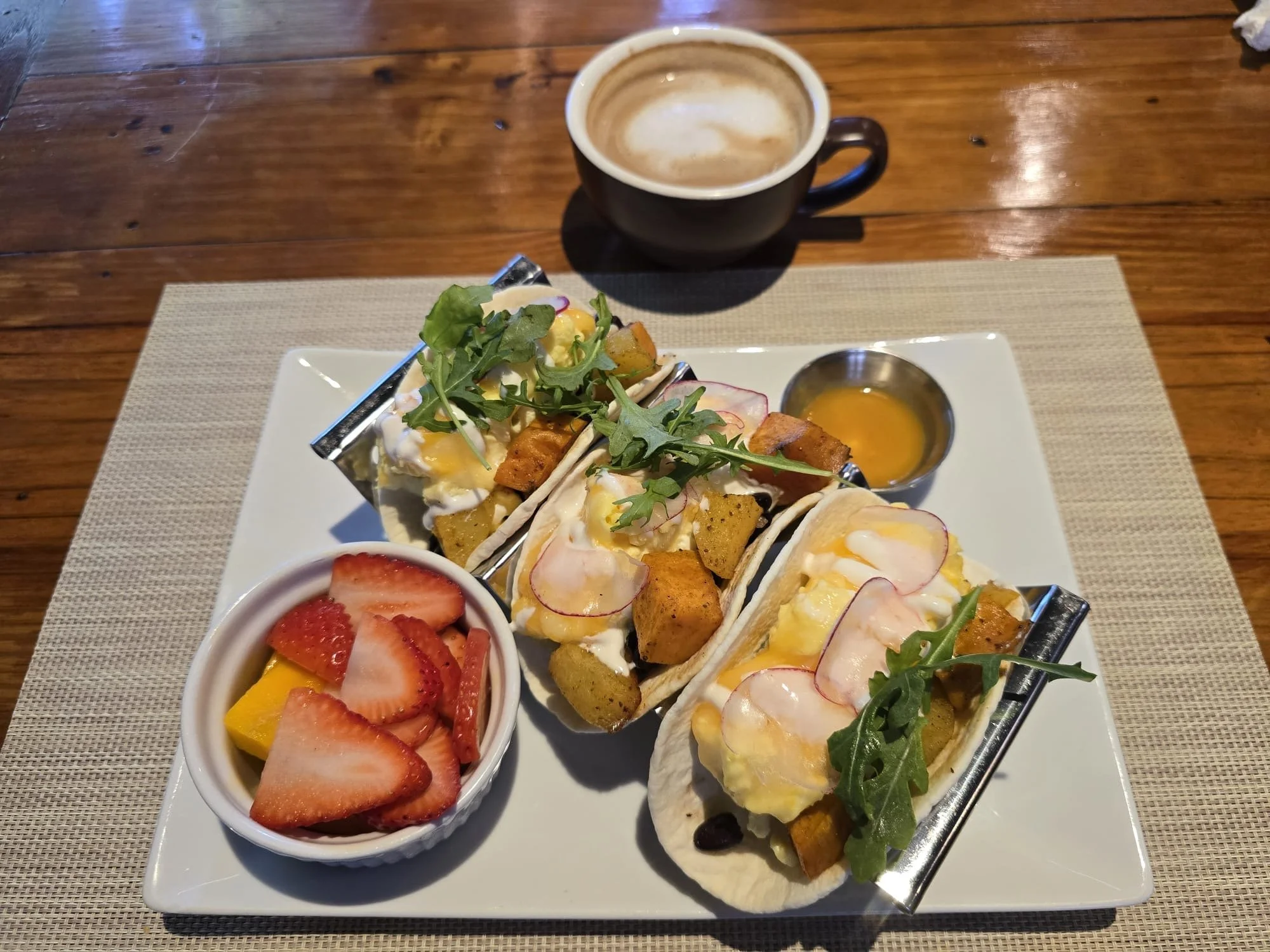 Breakfast tacos filled with scrambled eggs and roasted sweet potatoes, topped with fresh greens and radishes, served with fresh fruit